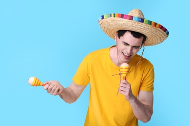 Photo of Young man in Mexican sombrero hat with maracas on light blue background