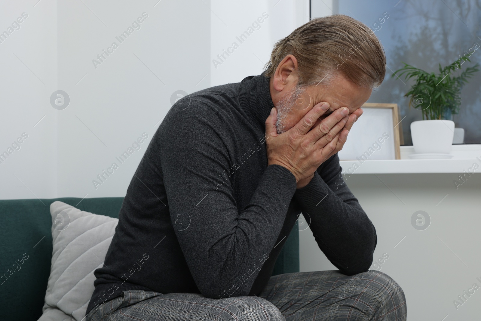 Photo of Upset senior man crying on sofa at home. Loneliness concept