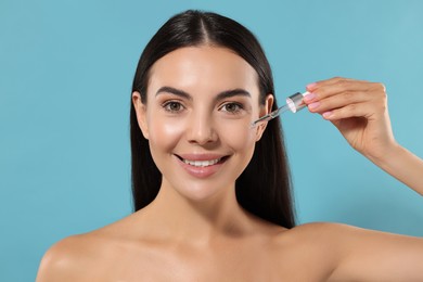 Photo of Beautiful young woman applying serum onto her face on light blue background