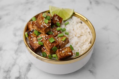 Photo of Bowl of rice with fried tofu and green onions on white marble table, closeup