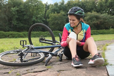 Photo of Young woman applying bandage onto her knee near bicycle outdoors