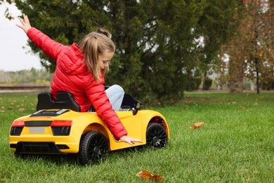Photo of Cute little girl driving children's car in park. Space for text