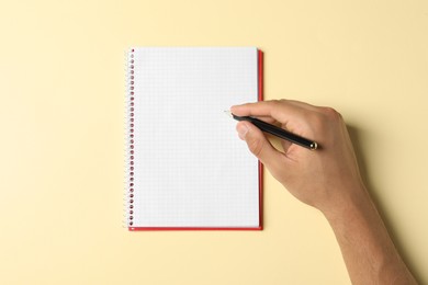 Photo of Man with pen and notepad on pale yellow background, top view