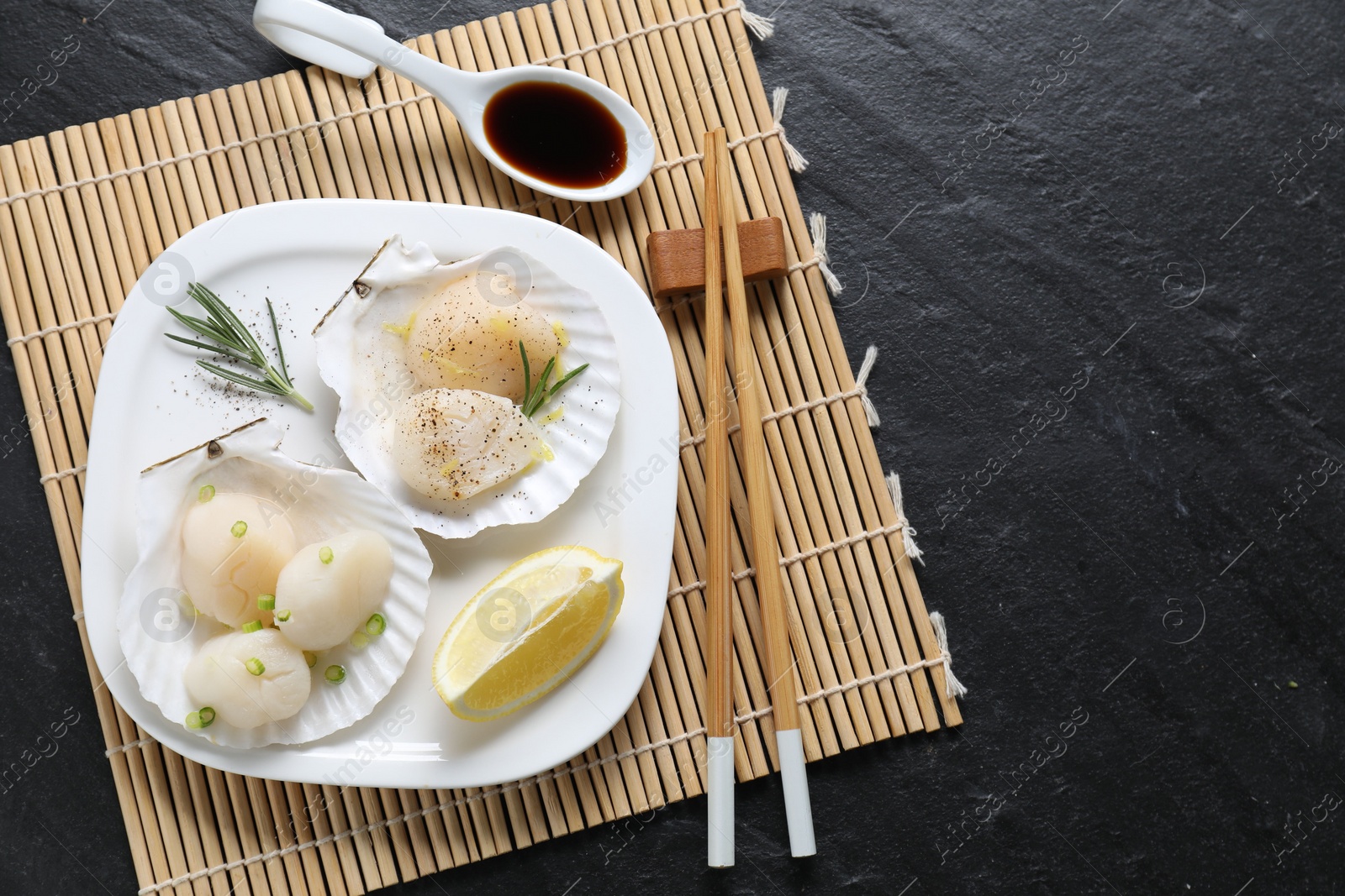 Photo of Raw scallops with green onion, rosemary, lemon and soy sauce on dark textured table, top view. Space for text