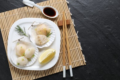 Photo of Raw scallops with green onion, rosemary, lemon and soy sauce on dark textured table, top view. Space for text
