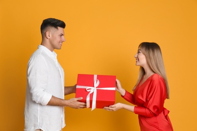 Photo of Lovely couple with gift on yellow background. Valentine's day celebration