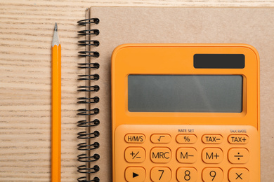 Photo of Calculator, notebook and pencil on wooden table, top view. Tax accounting
