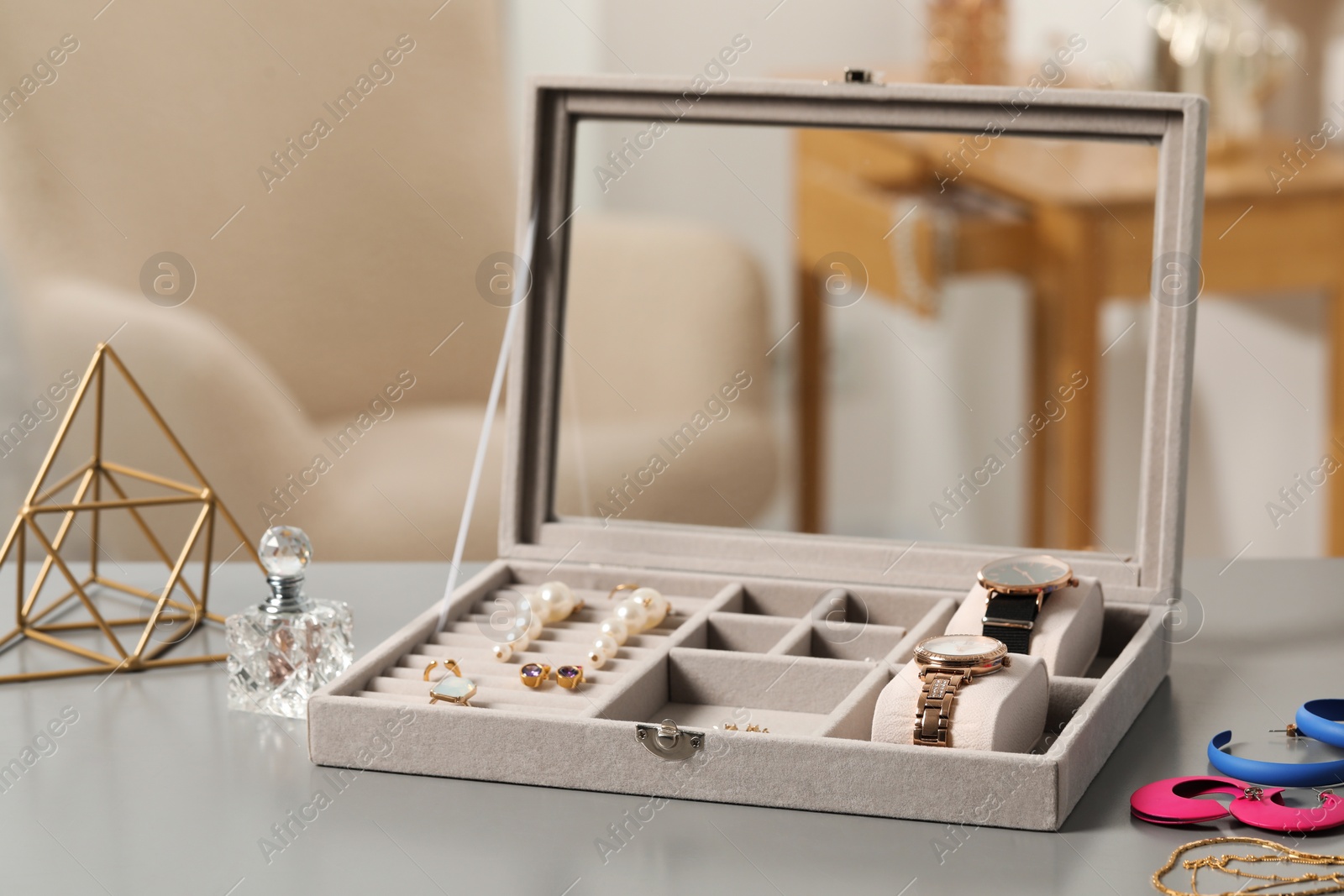 Photo of Jewelry box with many different accessories, perfume and decor on light grey table indoors