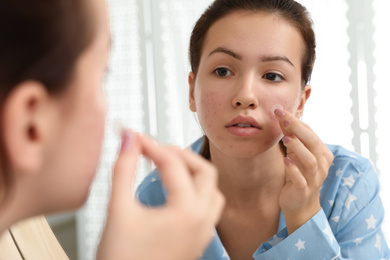 Photo of Teen girl applying acne healing patch near mirror in bathroom