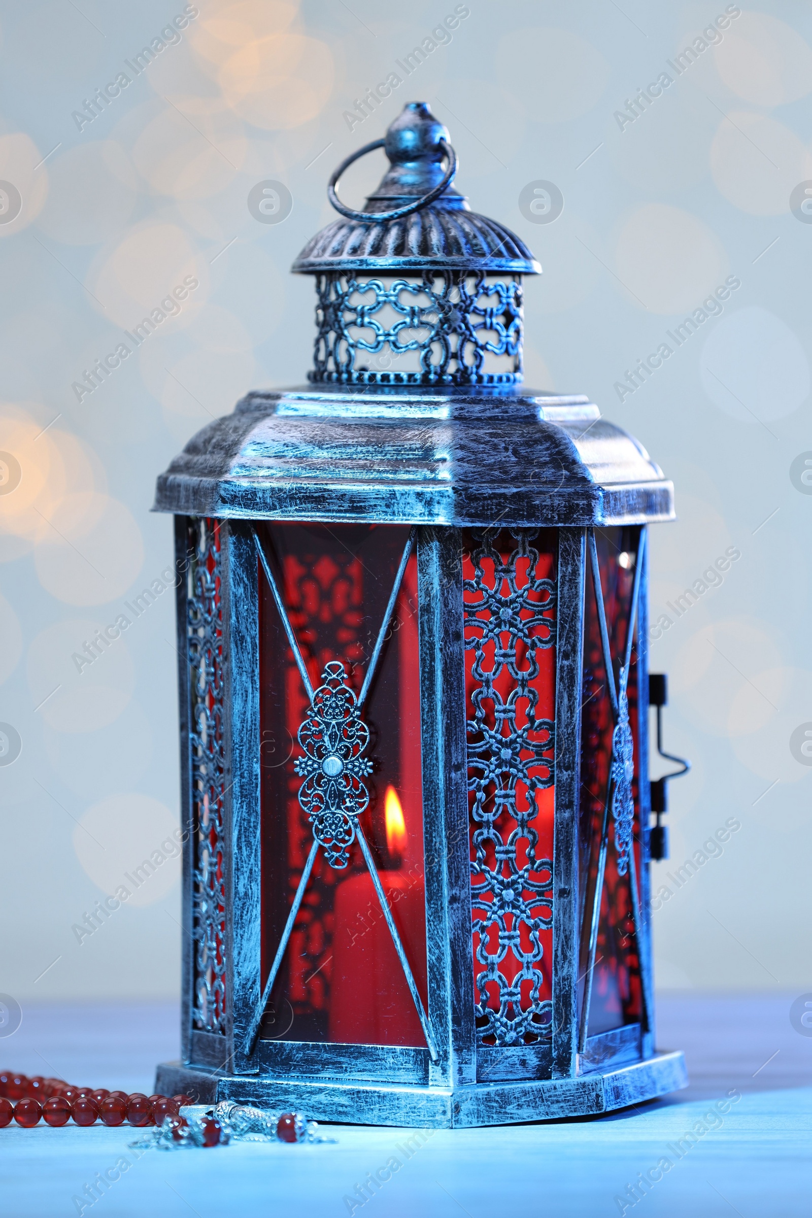 Photo of Arabic lantern and misbaha on table against blurred lights