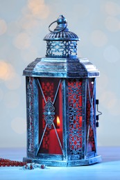 Photo of Arabic lantern and misbaha on table against blurred lights