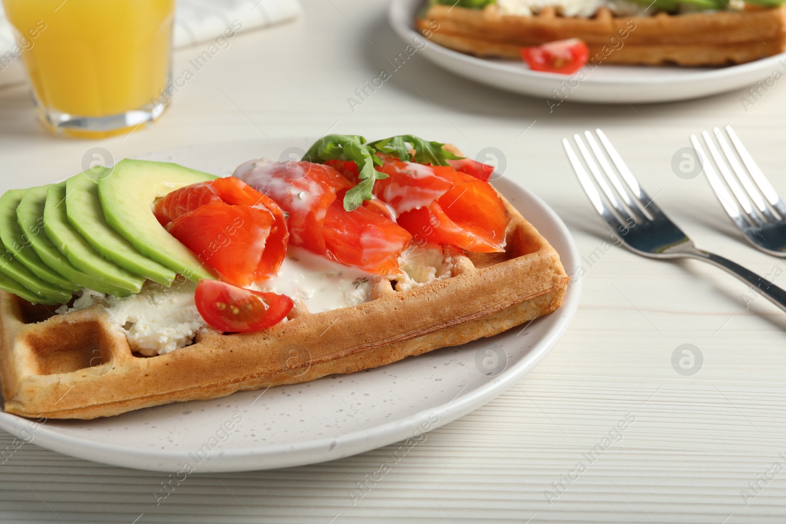 Photo of Delicious Belgian waffle with salmon, avocado and arugula on white wooden table