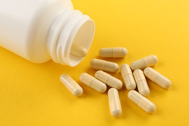 Photo of Bottle and vitamin capsules on yellow background, closeup