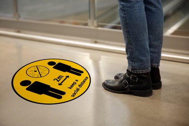 Image of Keep social distance as preventive measure during coronavirus outbreak. Yellow warning sign on floor in front of woman, closeup