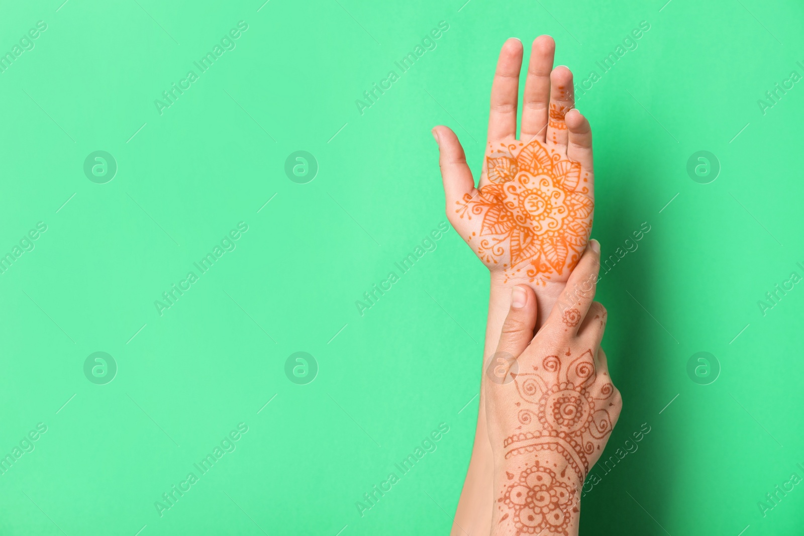 Photo of Woman with henna tattoos on hands against green background, closeup and space for text. Traditional mehndi ornament