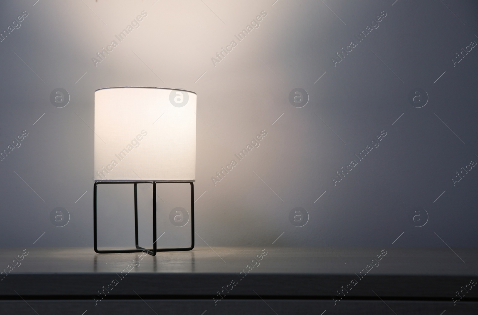 Photo of Wooden chest of drawers with modern lamp near light grey wall, space for text. Interior element