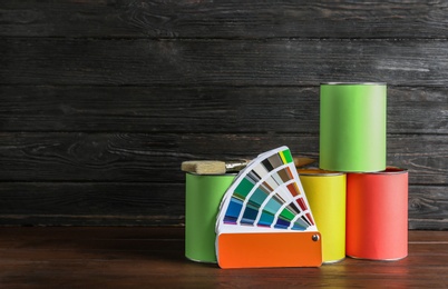 Photo of Paint cans, brush and color palette on table against wooden background. Space for text
