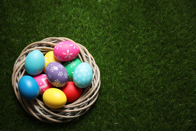 Photo of Colorful Easter eggs in decorative nest on green grass, top view. Space for text