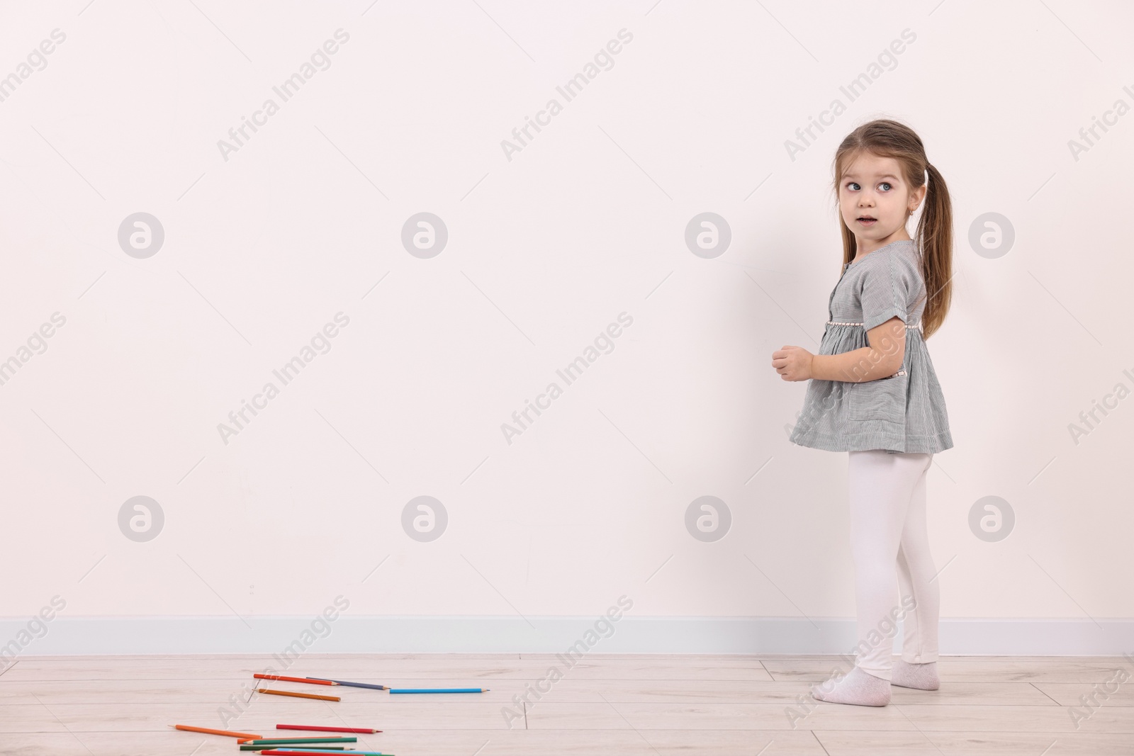 Photo of Little girl drawing on white wall indoors. Space for text