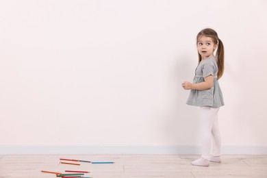 Little girl drawing on white wall indoors. Space for text