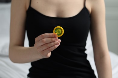 Woman holding unpacked condom on light background, closeup. Safe sex