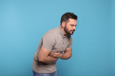 Photo of Unhappy man suffering from stomach pain on light blue background