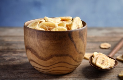 Photo of Bowl and spoon with sweet banana slices on wooden table. Dried fruit as healthy snack