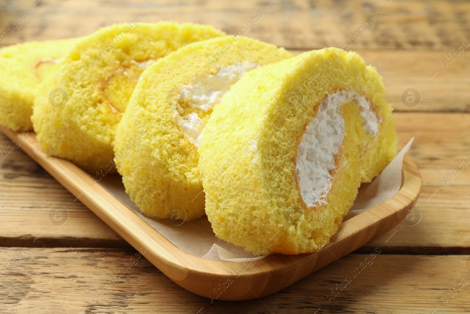 Photo of Delicious cake roll with cream filling on wooden table, closeup