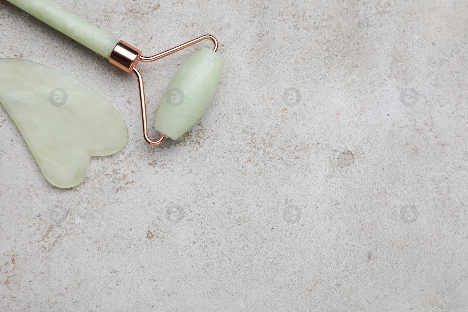Photo of Gua sha stone and face roller on light table, flat lay. Space for text