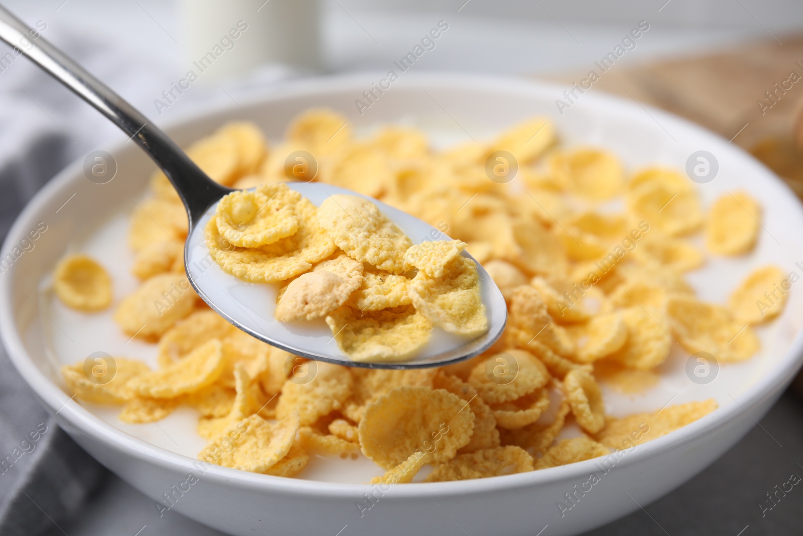 Photo of Breakfast cereal. Eating corn flakes and milk with spoon from bowl on table, closeup