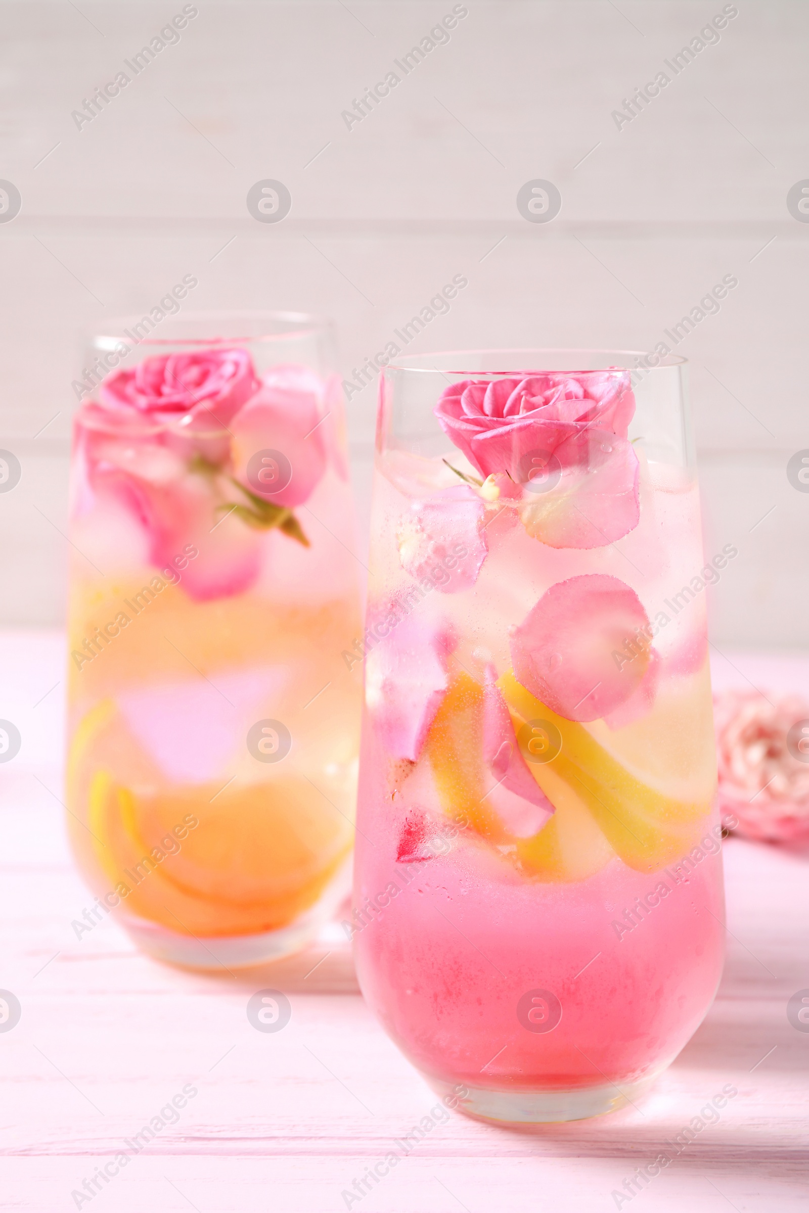 Photo of Delicious refreshing drink with lemon and roses on pink wooden table