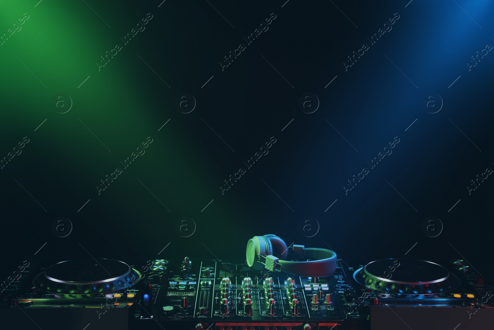 Photo of Modern DJ controller and headphones under beams of light on black background