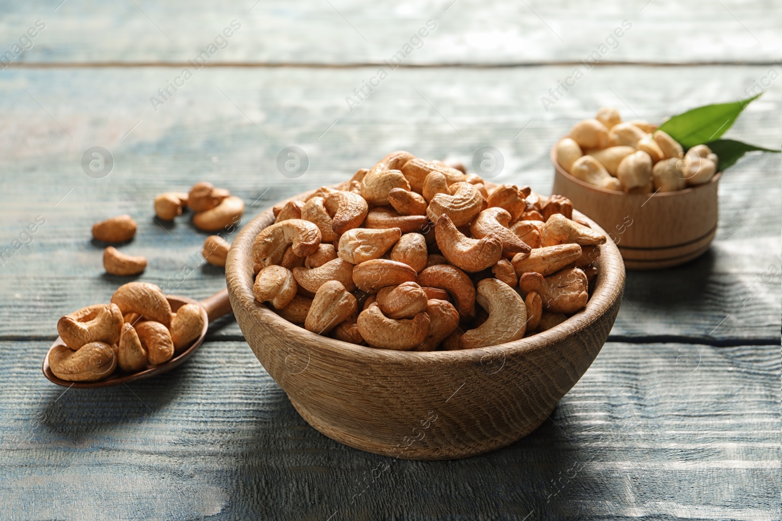 Photo of Tasty cashew nuts in bowl and spoon on wooden table
