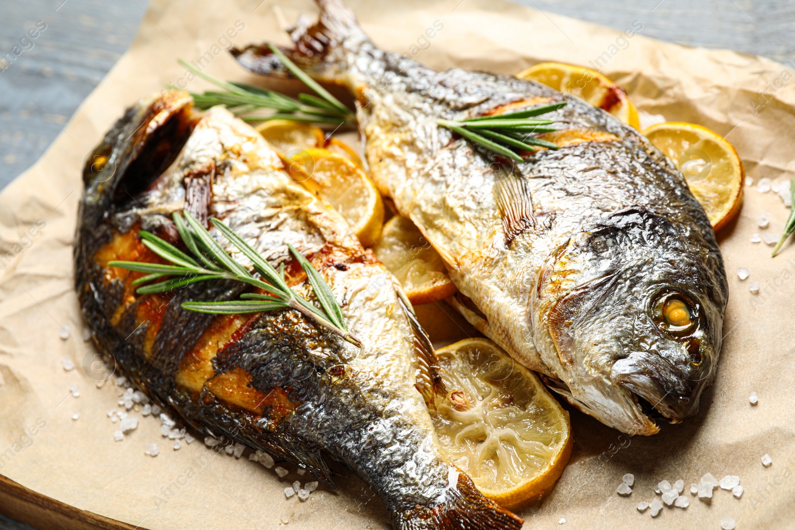 Photo of Delicious roasted fish with lemon on parchment paper, closeup