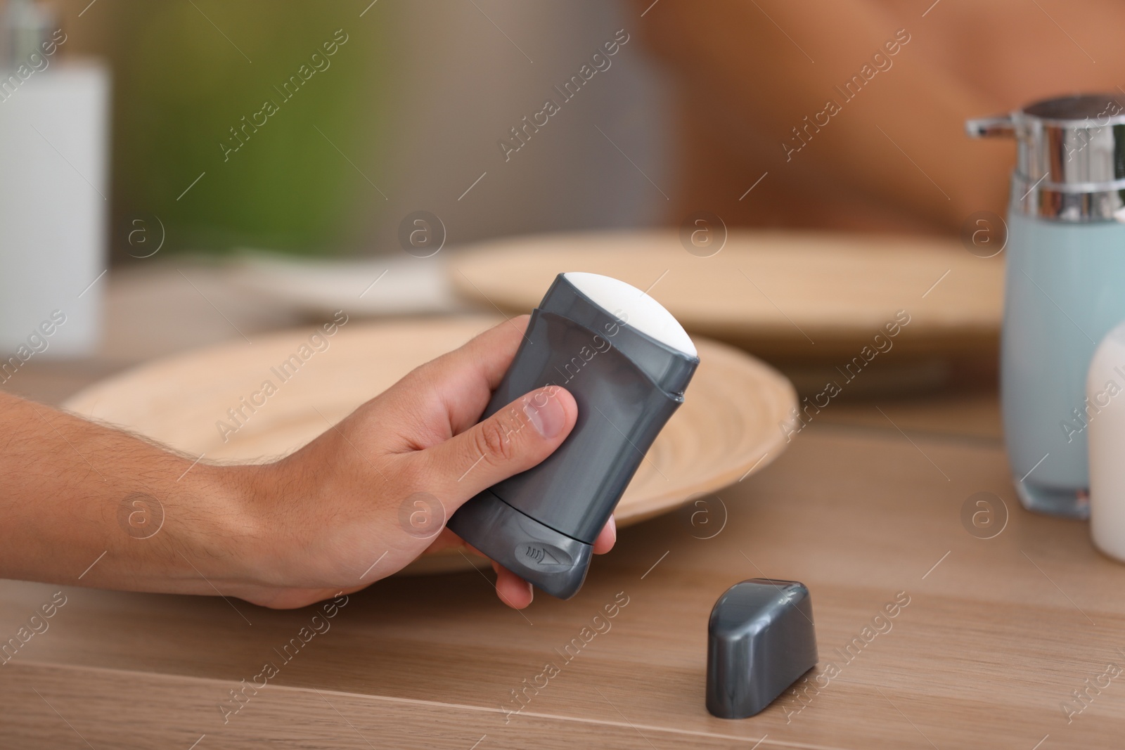 Photo of Young man holding deodorant over table in bathroom, closeup