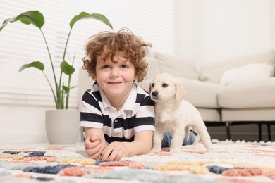 Photo of Little boy with cute puppy on carpet at home