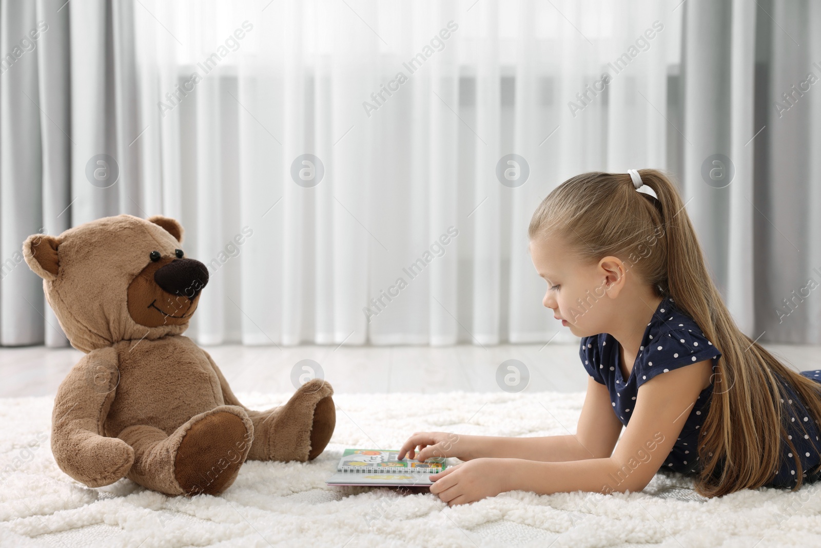 Photo of Cute little girl playing with teddy bear at home