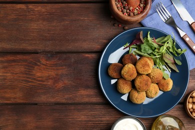 Photo of Delicious falafel balls with herbs served on wooden table, flat lay. Space for text