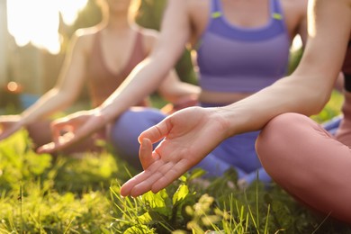 Photo of Women meditating on green grass outdoors, closeup. Morning yoga