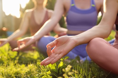 Women meditating on green grass outdoors, closeup. Morning yoga