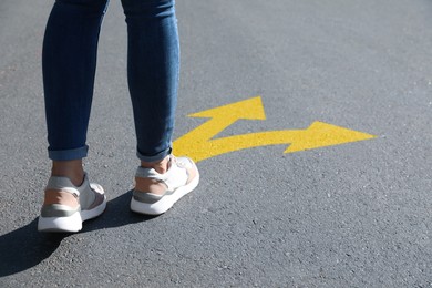 Image of Choice of way. Woman walking towards drawn mark on road, closeup. Yellow arrows pointing in different directions