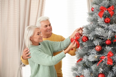 Happy mature couple decorating Christmas tree at home