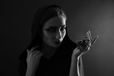 Photo of Mysterious witch with spooky spider on dark background. Black and white effect