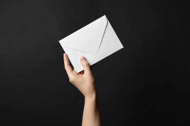 Woman holding white paper envelope on black background, closeup