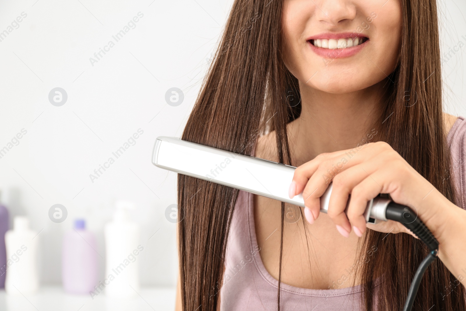 Photo of Young woman using hair iron indoors, closeup. Space for text