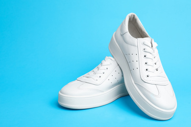 Photo of Stylish white shoes on light blue background. Space for text
