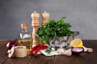 Photo of Colander with fresh parsley, spices and other products on wooden table