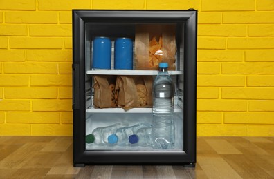 Photo of Mini bar filled with food and drinks near yellow brick wall indoors