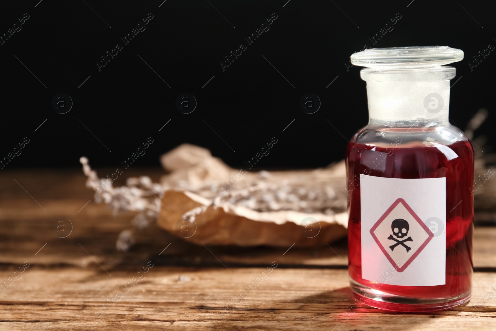 Photo of Glass bottle of poison with warning sign on wooden table. Space for text