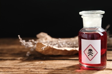 Photo of Glass bottle of poison with warning sign on wooden table. Space for text